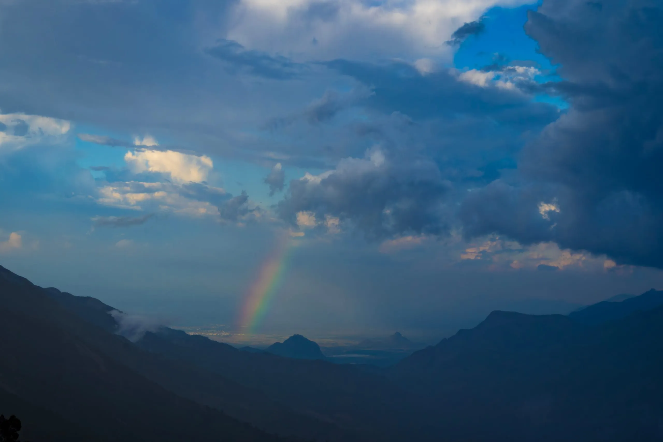 A rainbow standing over the plains, seen from above through a gap between two dark ridges